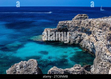 Wunderschönes Binibeca ein weißes, stilvolles Dorf an der Küste Menorcas, wo das blaue Meer die rauen Felsformationen berührt und Yachten friedlich vorbeisegeln Stockfoto