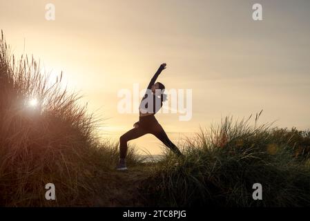 Frau, die draußen bei Sonnenaufgang Yoga macht, umgekehrte Kriegerposierung. Stockfoto