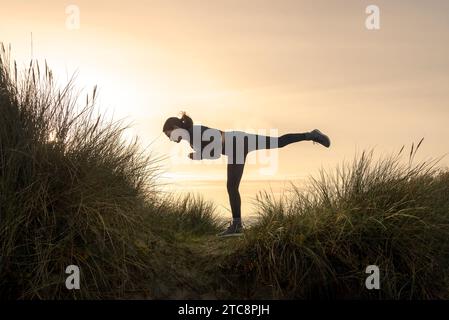 Seitenansicht einer Frau, die bei Sonnenaufgang Krieger III Yoga-Pose ausführt. Stockfoto