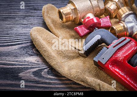 Leder-Sicherheitshandschuhe Affenschlüssel Messing Sanitäranschlüsse auf Holzplatte Stockfoto