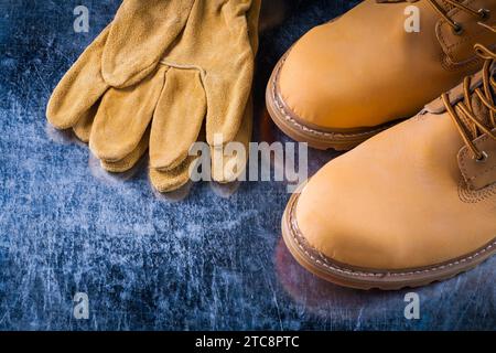 Schnürstiefel aus Leder und Schutzhandschuhe auf einem zerkratzten metallischen Hintergrund Stockfoto