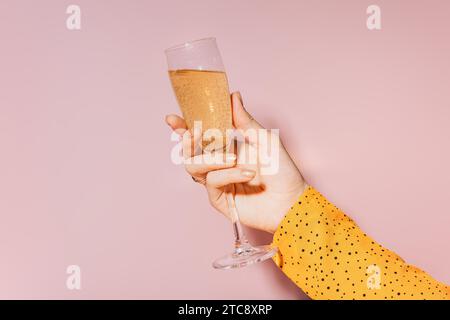 Eine Frauenhand mit goldbemalten Nägeln, die ein Glas Champagner auf rosa Hintergrund hält Stockfoto