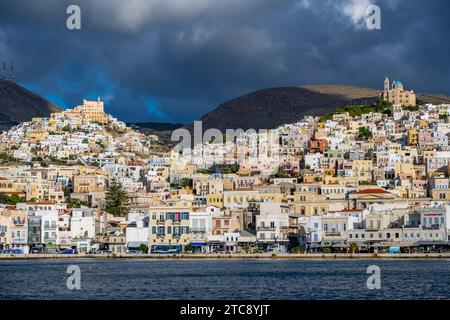 Blick auf die Stadt Ermoupoli mit pastellfarbenen Häusern und Meer, auf dem Hügel Anastasi Kirche oder Auferstehungskirche und Basilika San Stockfoto