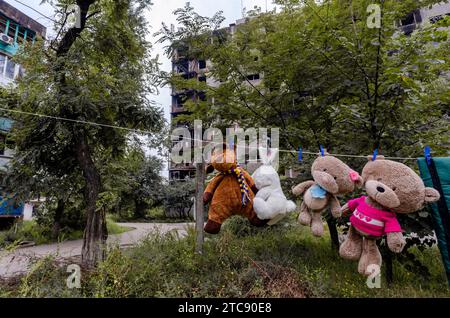 Kinderspielzeug hängt an einem Seil vor dem Hintergrund zerstörter verbrannter Häuser Krieg in der Ukraine mit Russland Stockfoto