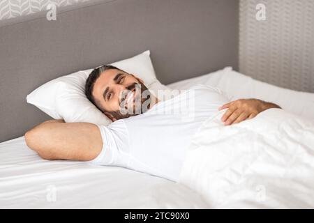 Entspannter europäischer Mann, der glücklich in einem komfortablen Bett im Schlafzimmer liegt Stockfoto