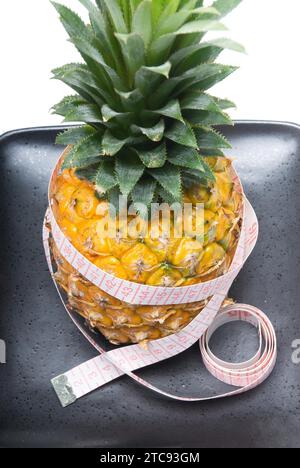 Ananas auf einer schwarzen Platte mit Bandmessgerät isoliert auf weißem Hintergrund Stockfoto