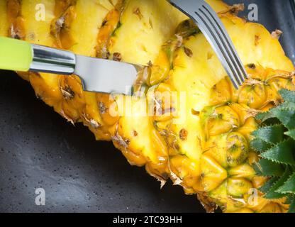 Reife, lebendige Ananas, geschnitten auf einem schwarzen Teller mit Messer und Gabel Stockfoto