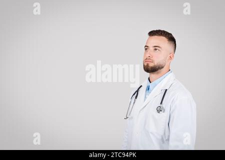Selbstbewusster männlicher Arzt in weißem Mantel, der auf freien Raum blickt Stockfoto