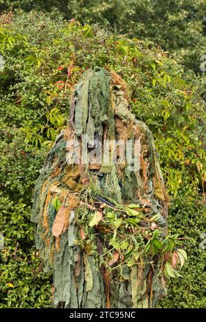 Ein Soldat, der ein militärisches Tarnoutfit trägt und sich in einen grünen Hintergrund einfügt Stockfoto