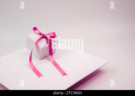 Eine kleine weiße Geschenkbox wird auf eine weiße quadratische Platte gelegt, die mit einem rosafarbenen Band gebunden ist Stockfoto