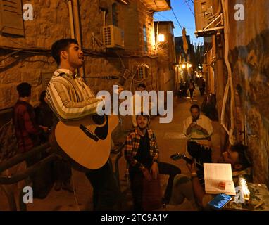 Jerusalem, Israel. Dezember 2023. Ein Mann spielt Gitarre und singt neben den Lichtern der Hanukkiya am Montag, den 11. Dezember 2023, in der fünften Nacht des jüdischen Feiertags von Hanukka, dem Lichterfest in Nachlaot in Jerusalem. Der achttägige Hanukka-Feiertag erinnert an den Sieg der Makkabäer über das griechisch-syrische Königreich und die Wiedereinweihung des Zweiten Tempels. Foto: Debbie Hill/ Credit: UPI/Alamy Live News Stockfoto