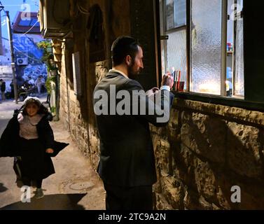 Jerusalem, Israel. Dezember 2023. Ein Ultra-orthodoxer Jude zündet eine Hanukkiya an der fünften Nacht des jüdischen Feiertags von Hanukka, dem Lichterfest, in Nachlaot in Jerusalem, am Montag, den 11. Dezember 2023. Der achttägige Hanukka-Feiertag erinnert an den Sieg der Makkabäer über das griechisch-syrische Königreich und die Wiedereinweihung des Zweiten Tempels. Foto: Debbie Hill/ Credit: UPI/Alamy Live News Stockfoto