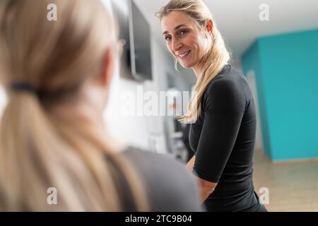 Die Kundin in einem Fitnessstudio unterhält sich während der Untersuchung mit einem Trainer, sie lächelt und ist fröhlich. Stockfoto