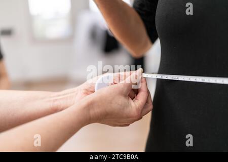 Nahaufnahme eines Fitnesstrainers, der die Taille einer Frau mit einem Maßband im Fitnessstudio misst. Bild des Fitness- und Gesundheitskonzepts Stockfoto