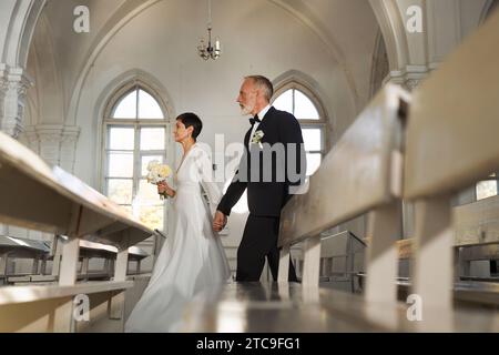 Seitliches Porträt eines älteren Ehepaares, das am Hochzeitstag gemeinsam den Kirchengang entlang läuft, Kopierraum Stockfoto
