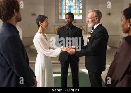 Seitliches Porträt eines älteren Paares als Braut und Bräutigam, der am Hochzeitstag mit Freunden und Familie Hände am Kirchenaltar hält Stockfoto