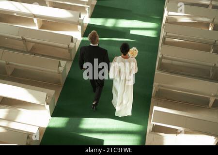 Blick von oben auf ein älteres Paar, das während der Hochzeitszeremonie im Sonnenlicht den Gang in der Kirche entlang geht, Kopierraum Stockfoto