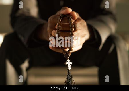 Nahaufnahme des Priesters, der hölzerne Rosenkranzperlen hält und in ätherischem Sonnenlicht betet, Kopierraum Stockfoto