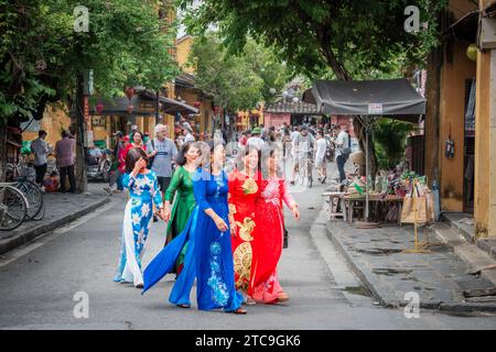 Hoi an, Vietnam, 20. November 2022: Eine Gruppe vietnamesischer Frauen in traditionellen Kleidern, die auf einer belebten Straße in Hoi an, Vietnam, spazieren Stockfoto