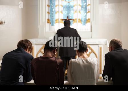 Rückansicht einer Gruppe junger Menschen, die während des Sonntagsgottesdienstes in der katholischen Kirche still beteten Stockfoto