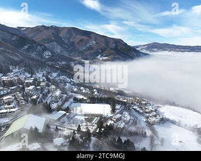 Ein idyllischer Blick aus der Vogelperspektive auf eine malerische Bergstadt, eingebettet zwischen üppig grünen Bergen und klarem blauem Himmel Stockfoto
