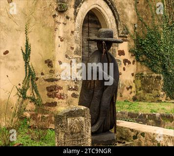 Landes, Frankreich - 30. November 2023 - Holzfigur vor einer alten Kirche in dunkler Farbe mit Hut Stockfoto