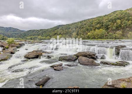 Eine atemberaubende Landschaft mit einem Wasserfall, der über Felsen und Bäume an einem Flussufer kaskadiert Stockfoto