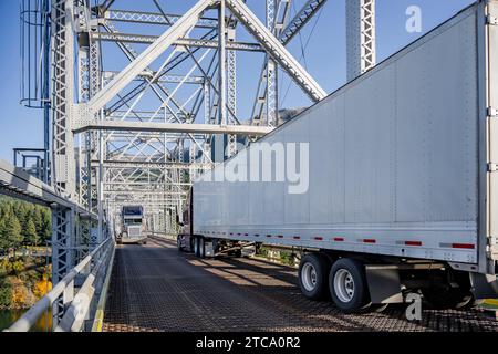 Langstreckenfahrzeug zwei industrielle große Sattelauflieger mit beladenen Aufliegern, die sich zueinander bewegten, trafen auf einer schmalen Fachwerkbrücke, die Schwierigkeiten hatte Stockfoto