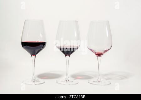 Drei Gläser mit je weniger Rotwein, isoliert auf weiß. Das Konzept des achtsamen Trinkens und der Alkoholreduzierung. Stockfoto