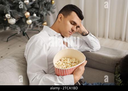 Betrunkener junger Mann mit Popcorn, der auf dem Sofa nach der Neujahrsfeier zu Hause schläft Stockfoto