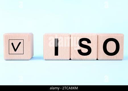 Internationale Organisation für Normung. Holzwürfel mit Häkchen und Abkürzung ISO auf hellblauem Hintergrund Stockfoto