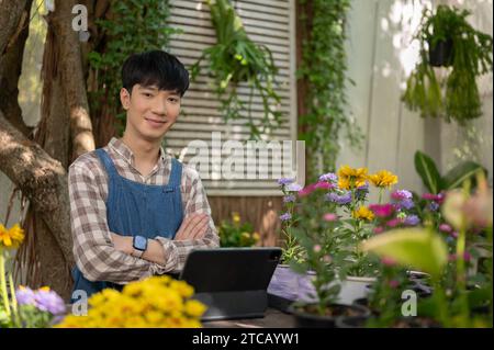 Ein Porträt eines hübschen, positiven jungen asiatischen Mannes, der Besitzer eines kleinen Blumenladens ist in seinem kleinen Garten. Florist, Gärtner, Blumenhändler, Unternehmer Stockfoto