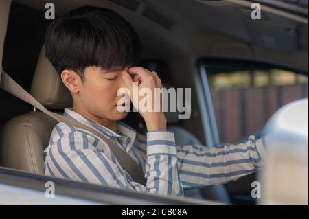 Ein müder junger asiatischer Mann leidet unter Kopfschmerzen oder Augenanstrengung, während er stundenlang im Auto fährt. Personen- und Fahrzeugkonzepte Stockfoto