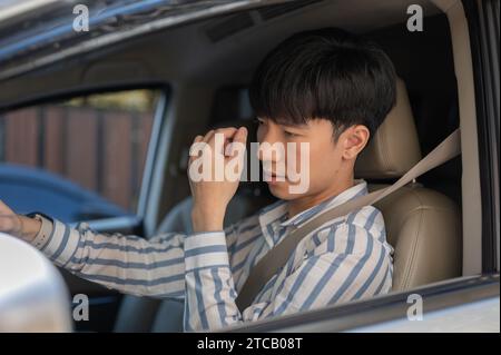 Ein müder junger asiatischer Mann leidet unter Kopfschmerzen oder Augenanstrengung, während er stundenlang im Auto fährt. Personen- und Fahrzeugkonzepte Stockfoto