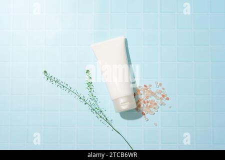 Ein leeres Kosmetikröhrchen wird auf einem karierten blauen Hintergrund mit rosafarbenem Himalaya-Salz platziert. Konzept der Hautreinigung mit Naturkosmetik - sicher und Stockfoto