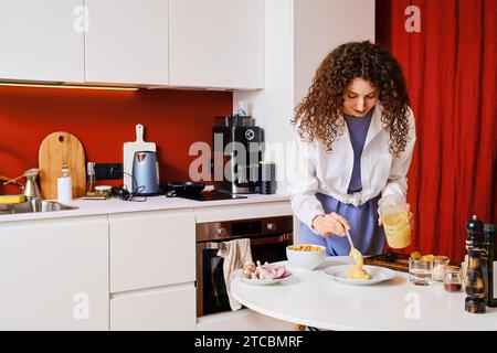 Die junge Frau legt Hummus auf den Teller. Handgemachte frische Speisen. Stockfoto