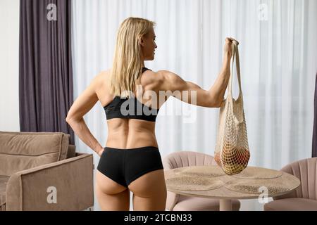 Rückansicht einer muskulösen Frau, die Obst und Gemüse im Einkaufstasche hält Stockfoto