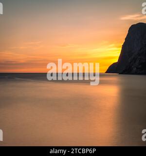 Ein malerischer Blick auf einen lebendigen Sonnenuntergang über dem Meer mit einer großen Felsformation in Lofoten, Norwegen Stockfoto