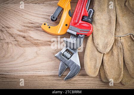 Leder Schutzhandschuhe einstellbarer Schraubenschlüssel Affenschlüssel Rohrschneider auf Holzbrett Sanitärkonzept Stockfoto