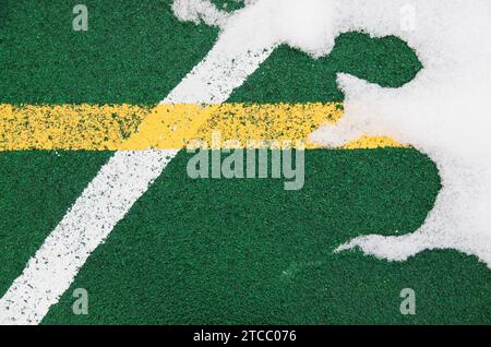 Eine Nahaufnahme ist ein spezialisierter Outdoor-Sportplatz, der eine grüne Gummikrümel mit markierten Linien für Sport bedeckt. Mit Schnee bedeckt. Die Stockfoto