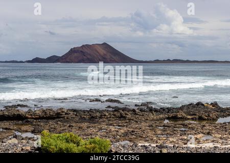 Panoramablick auf die Küste von Corralejo auf der kanarischen Insel Fuerteventura, Spanien mit Lavafelsen und rauem Meer mit Wellen und Insel Isla de Lobos Stockfoto