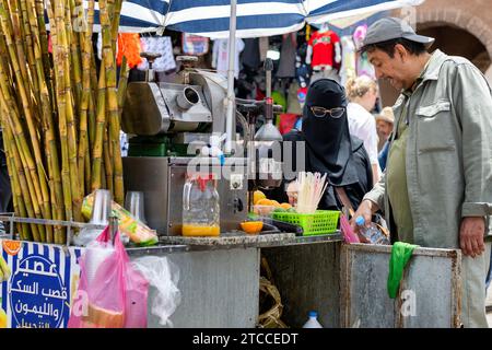 Essaouira, Marokko: Marokkanische Frau mit schwarzem Niqab kauft einen Fruchtsaft auf einer Medina-Straße. Stockfoto