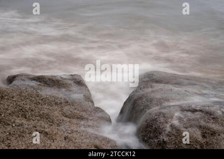 Langsame Aufnahmen der Meereswellen entlang des felsigen Strandes. Stockfoto