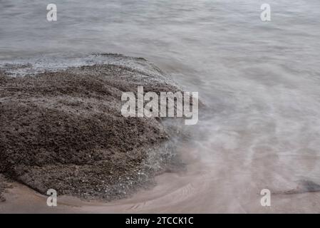 Langsame Aufnahmen der Meereswellen entlang des felsigen Strandes. Stockfoto