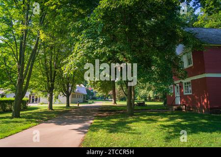 Ein sonnendurchfluteter gepflasterter Weg windet sich durch einen schattigen Hain von Laubbäumen hin zu einem roten Schindelhaus am James A. Garfield National Historic Site, Ohio. Stockfoto