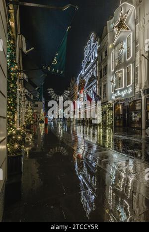 Luxusgeschäfte reflektieren die leere Straße bei nächtlichem Regen in Mayfair, London. Stockfoto