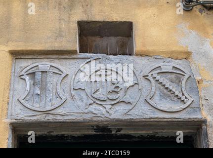 Steinrelief mit dem religiösen Symbol JHS zwischen zwei Wappen im mittelalterlichen Dorf Finalborgo, Finale Ligure, Savona, Ligurien, Italien Stockfoto