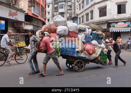 Vier Männer schieben und ziehen einen schwer beladenen Handwagen entlang der Kalbadevi Road, im Handels- und Geschäftsviertel Bhuleshwar, Mumbai, Indien Stockfoto