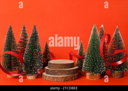 Festliche Weihnachtsszene Podium für Produktpräsentation, Werbeverkauf, grüne Weihnachtsbäume mit hölzernem Podium auf rotem Hintergrund Stockfoto