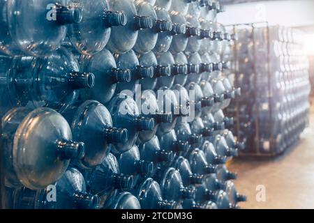 Trinkwasser-saubere Gallonen-Flaschen stapeln sich im Lagerlager in der Trinkwasserfabrik und warten in der Schlange auf die Wasserabfüllung im Werk. Stockfoto